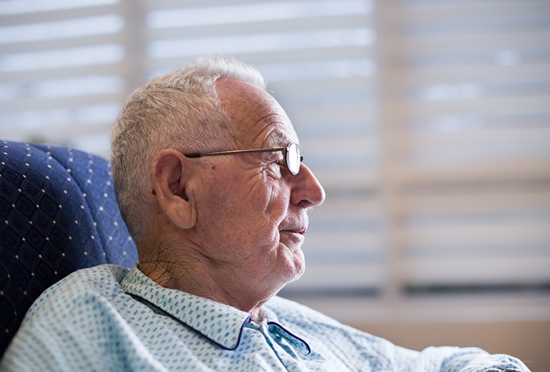 Portrait of smiling old man in pajamas sitting on sofa and looking at tv