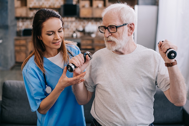 Physical Therapist assisting patient with small hand weights during short term therapy session