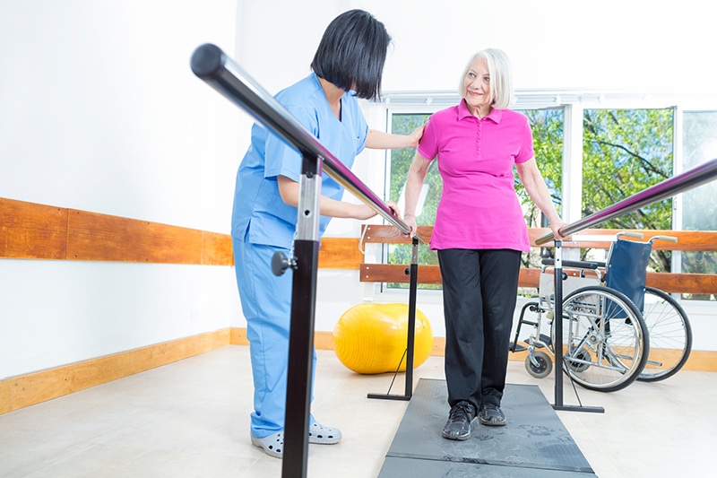 Physical Therapist standing next to short term rehab patient using stability bars to walk during therapy session.