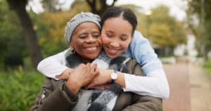 older woman resident at a skilled nursing facility in Denison, TX being hugged by a young staff member outside on a trail